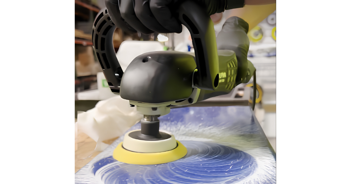 Black and gray ALPHA variable speed rotary polisher with a yellow pad on a blue surface with a blurred background
